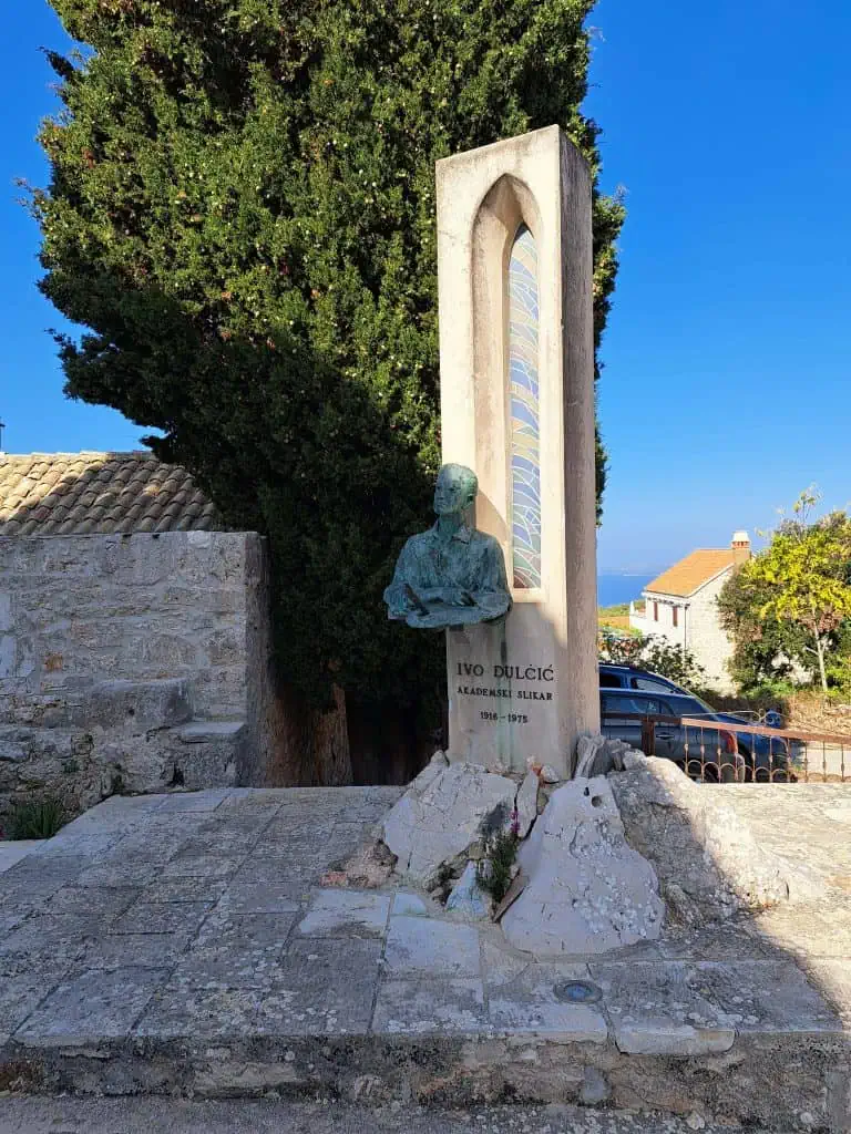 Stone memorial with a bust beside a cypress in Brusje