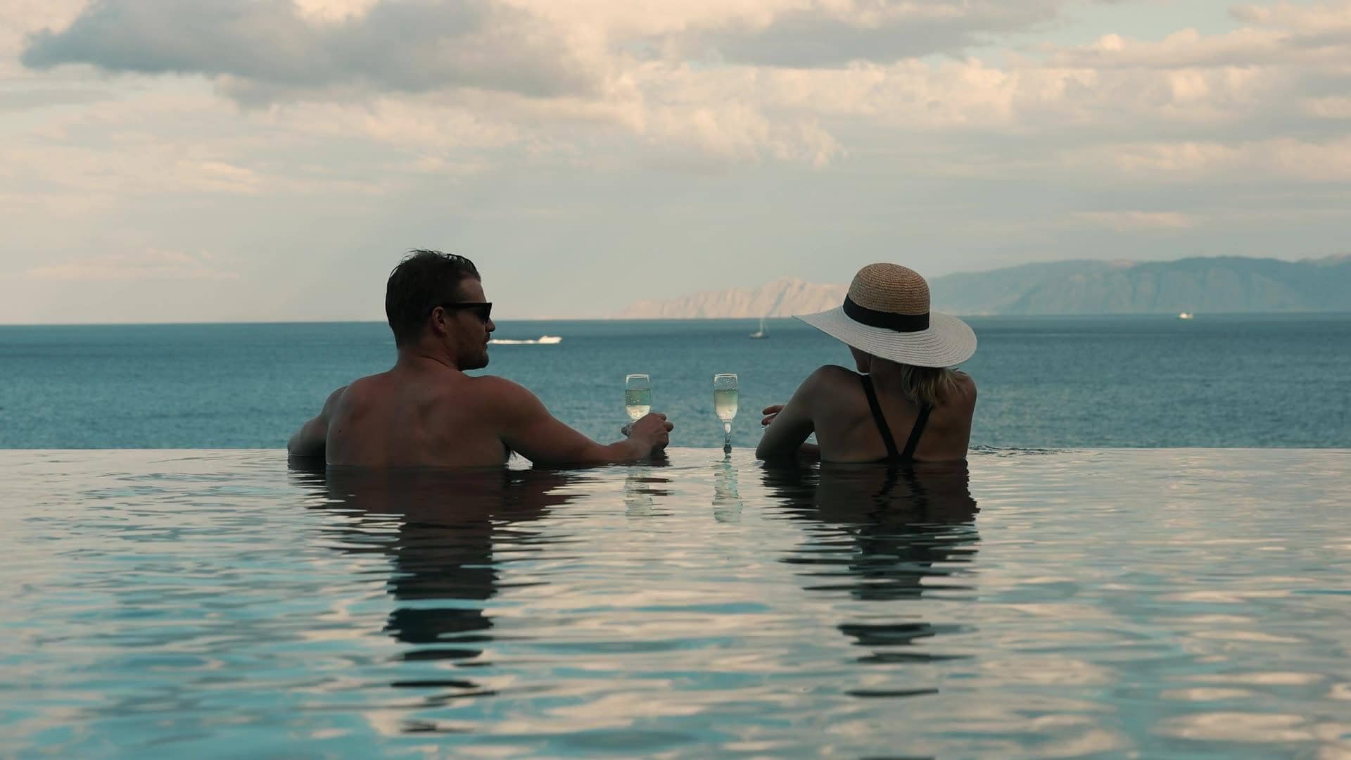 Couple in the infinity pool of a Hvar villa with sparkling wine, looking out over the Adriatic at sunset, island of Hvar, Croatia