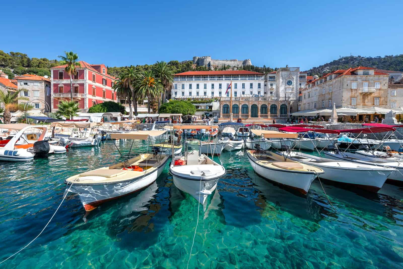 Small boats moored along the Hvar Town waterfront, with the Arsenal, the main square and the Fortica fortress behind