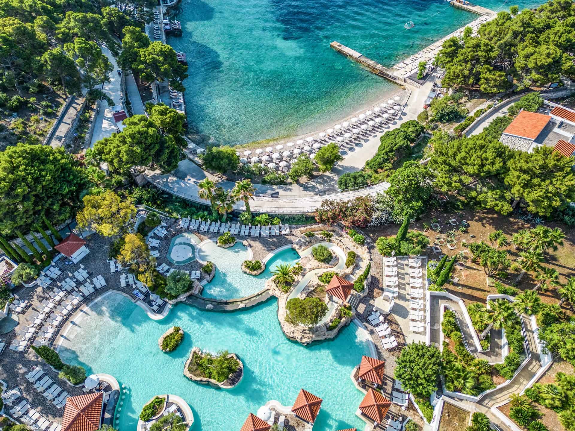 The cascading pool of the Amfora resort seen from the air, curving around planted islands above a pine-lined bay